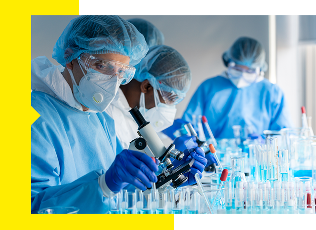 Group of researchers in protective gear analyzing contents of a test tube.